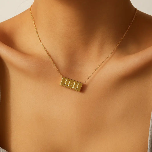 Gold necklace with a rectangular pendant on a person's neck against a neutral background