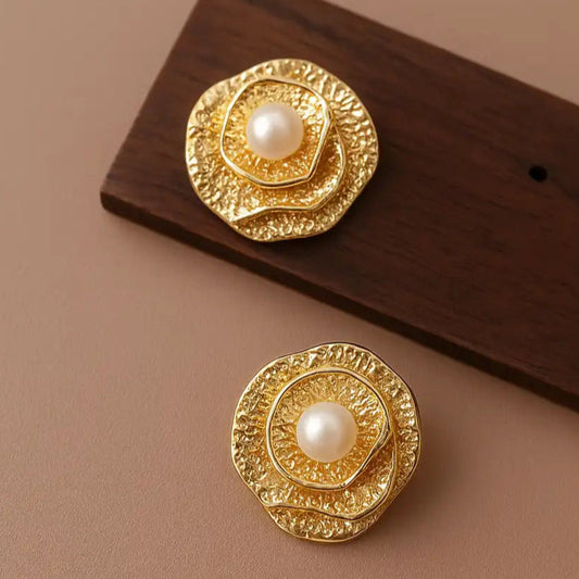 Gold brooches with pearl centers on a brown surface
