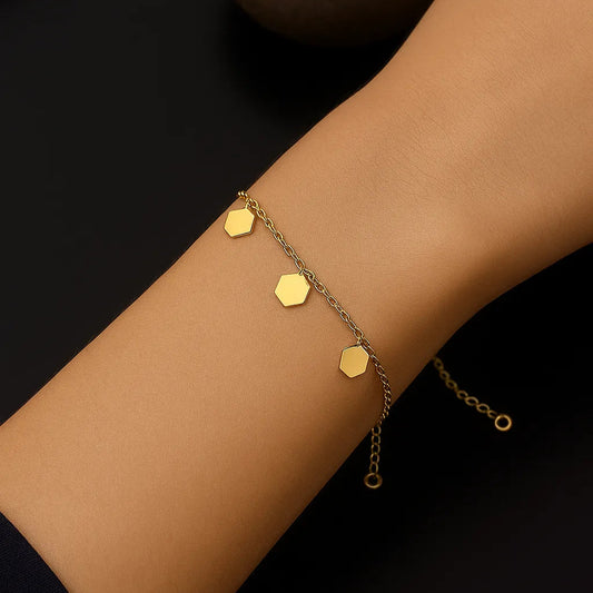Gold bracelet with hexagonal charms on a wrist against a dark background