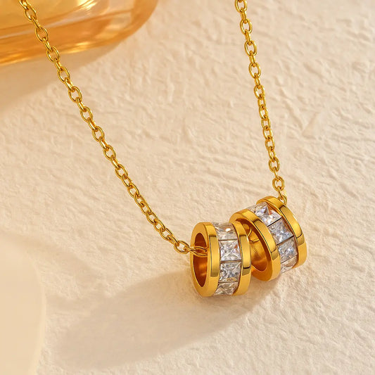 Gold necklace with a cylindrical pendant featuring diamonds on a beige background