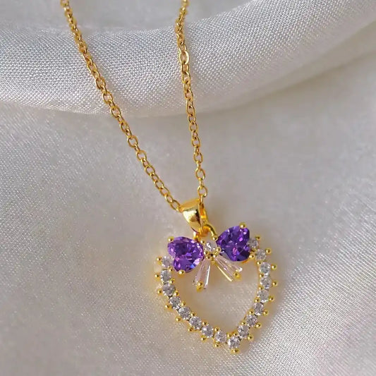 Gold necklace with a heart-shaped pendant featuring purple gemstones on a white fabric background