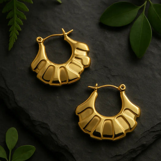 Gold hoop earrings on a dark surface with green leaves