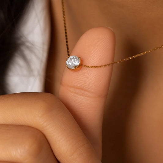 Gold necklace with a diamond pendant held between fingers against a blurred background