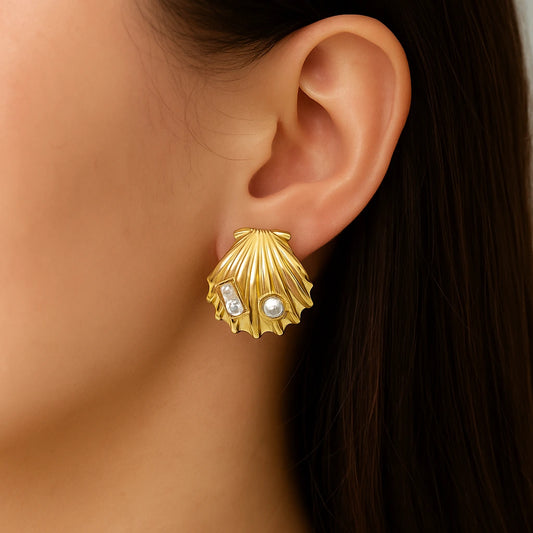 Gold shell-shaped earring with embedded pearls worn by a person.