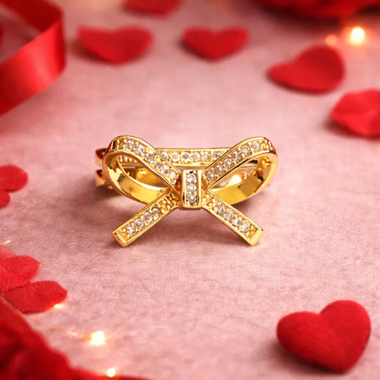 Gold bow-shaped ring on a pink surface with red roses and heart shapes.