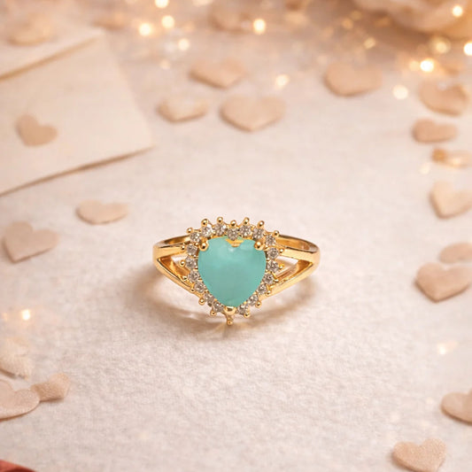 Gold ring with a turquoise heart-shaped gemstone on a soft background with lights and ribbons.