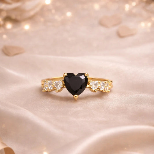 Gold ring with a black heart-shaped gemstone on a soft, light-colored fabric background.