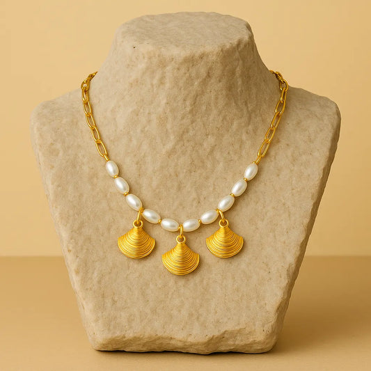 Gold necklace with shell pendants on a stone mannequin against a beige background