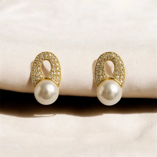Pair of pearl earrings with gold and diamond accents on a beige surface
