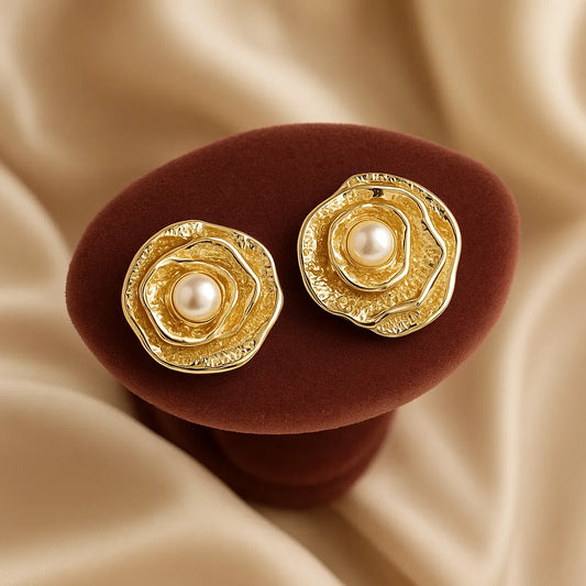 Gold earrings with pearls on a brown stand against a beige fabric background