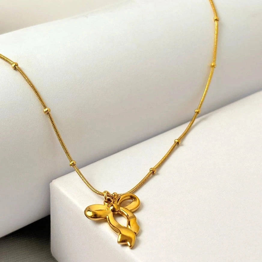 Gold necklace with a bow pendant on a white surface