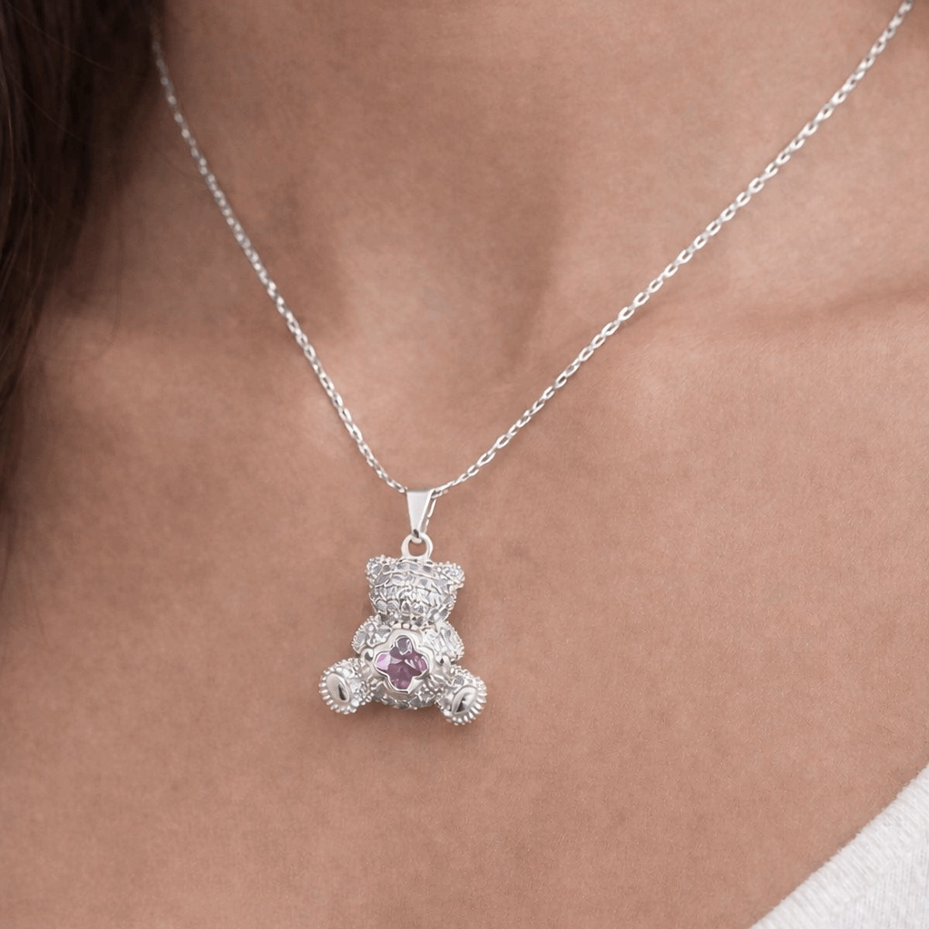 Silver teddy bear pendant necklace with a pink gemstone on a person's neck.