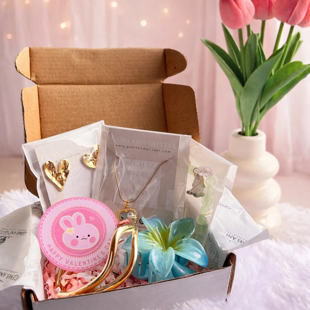 Gift box with jewelry and stationery items on a soft pink background with tulips.