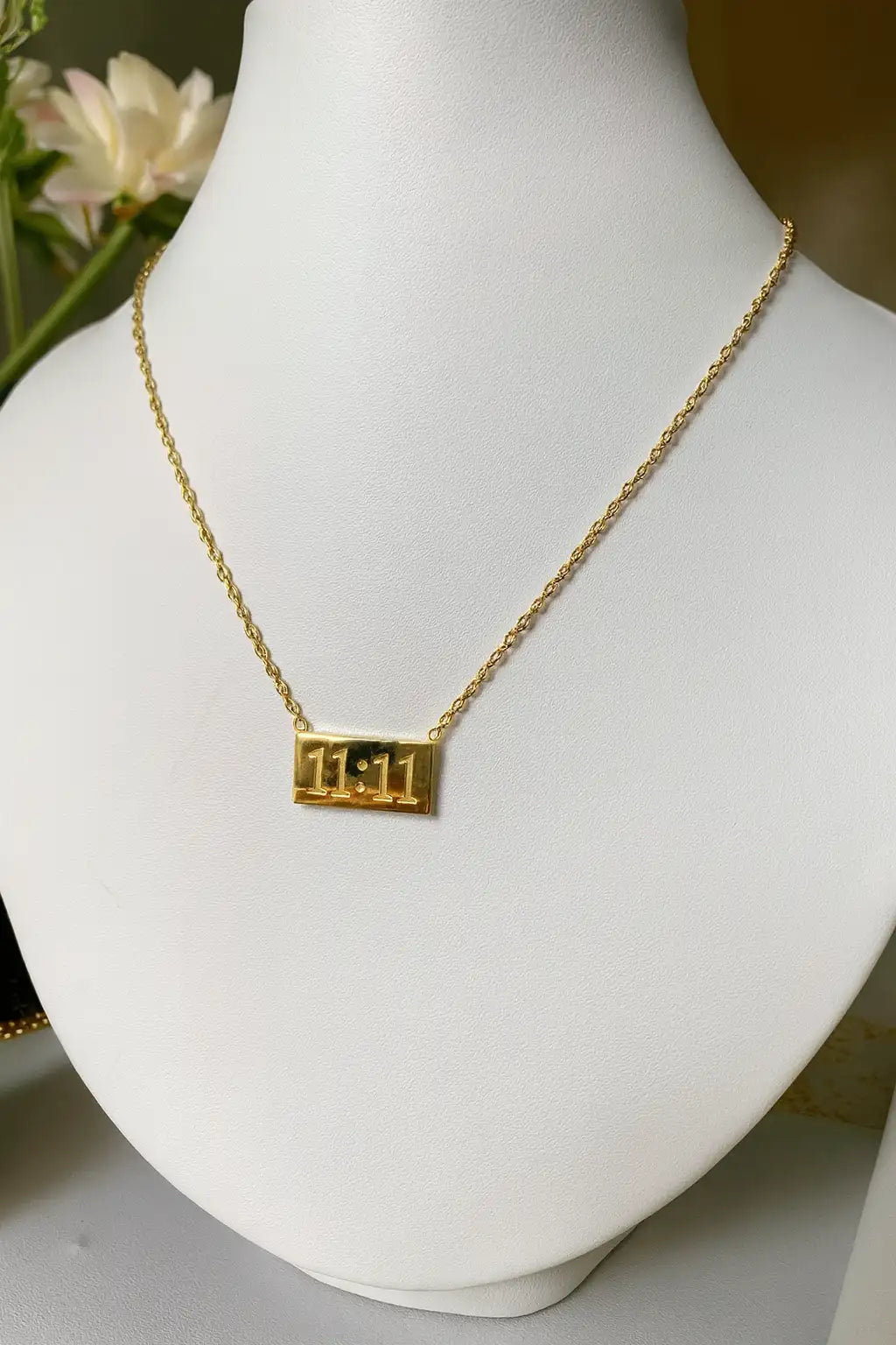 Gold necklace with a rectangular pendant on a white mannequin bust.