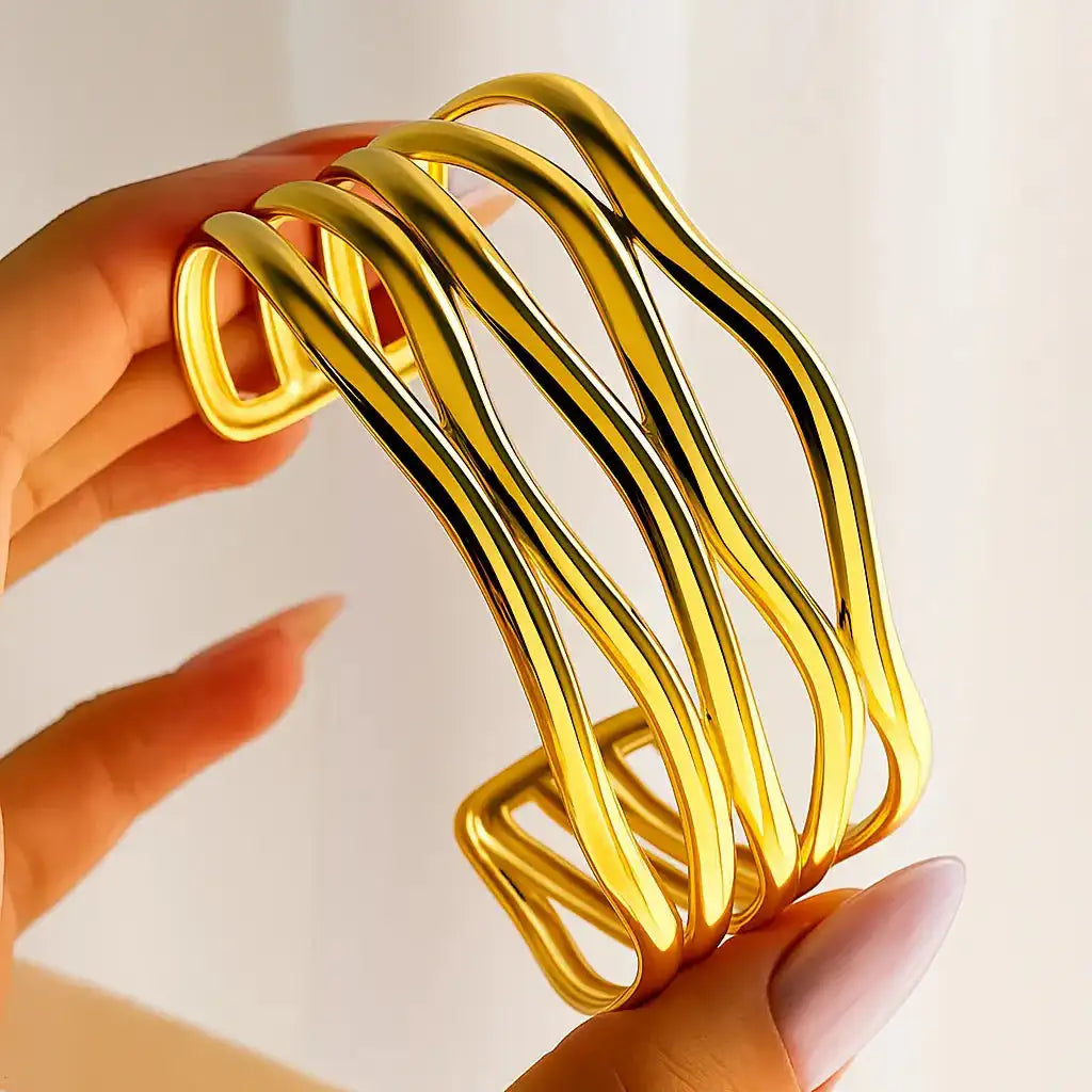 Gold bracelet held by a hand against a light background