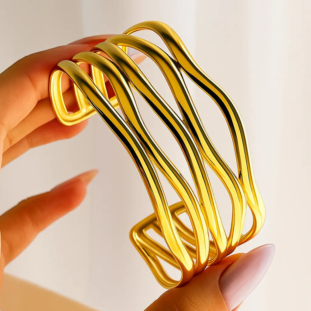 Gold bracelet held by a hand against a light background