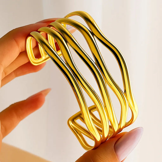 Gold bracelet held by a hand against a light background
