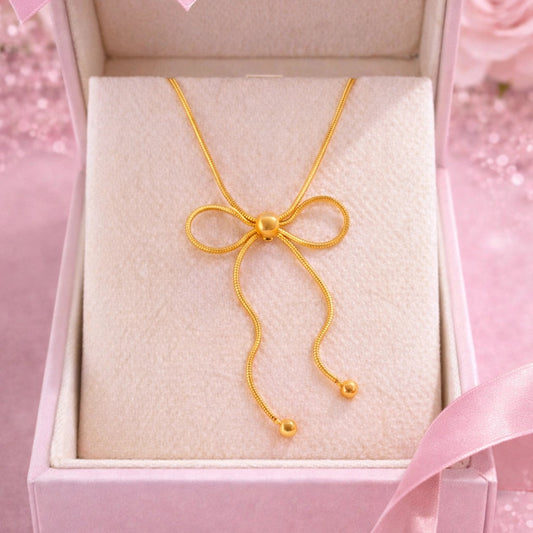 Gold bow-shaped necklace in a pink box with a pink ribbon