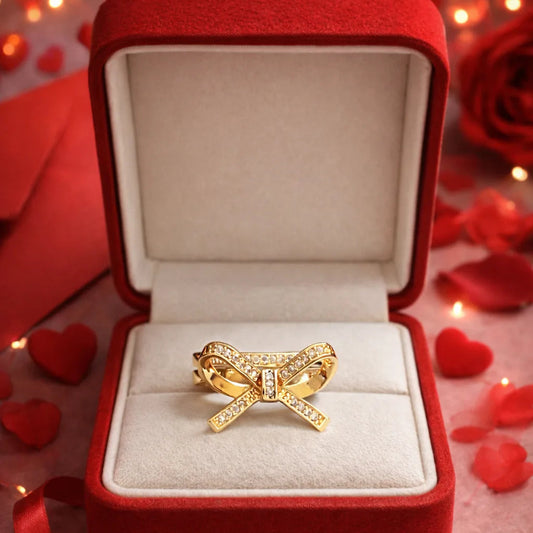 Gold bow-shaped ring in a red box with heart-shaped decorations
