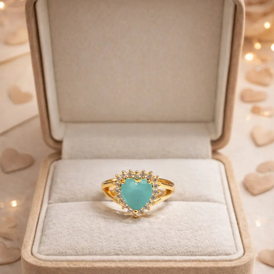 Turquoise heart-shaped ring with gold accents in a jewelry box on a decorative background.
