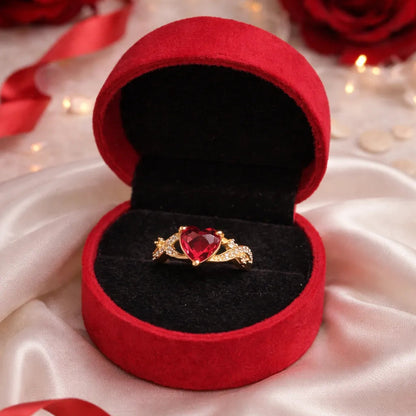 Red velvet ring box with a heart-shaped ring on a white fabric background with red ribbons.