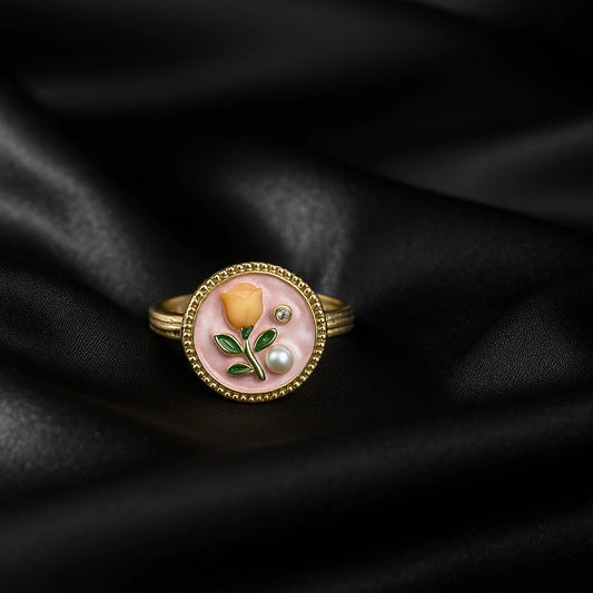 Gold ring with a pink stone featuring a yellow rose design on black fabric