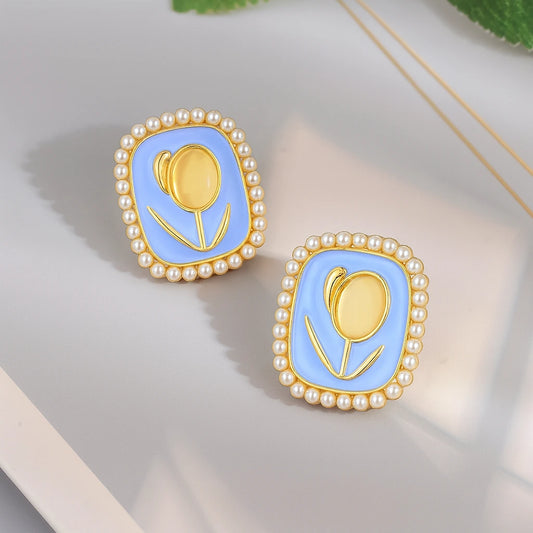 Pair of earrings with gold tulip design and pearl border on a light background