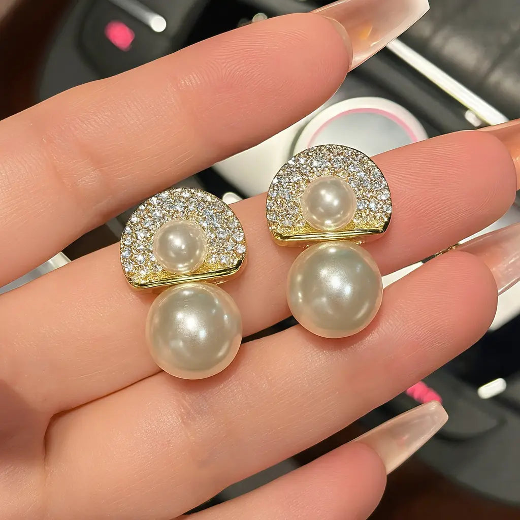 Pearl earrings with gold accents held between fingers against a blurred background