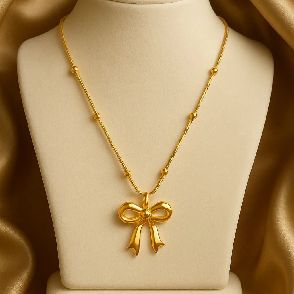 Gold necklace with a bow pendant on a beige mannequin bust against a gold satin background
