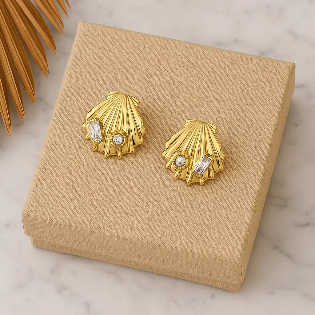 Gold shell-shaped earrings with embedded stones on a beige jewelry box.