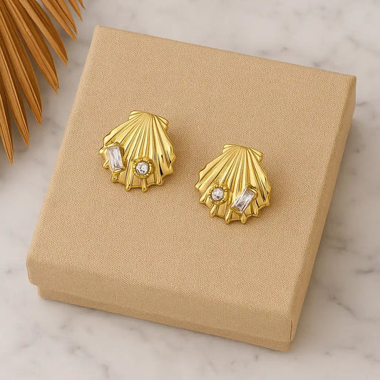 Gold shell-shaped earrings with embedded stones on a beige jewelry box.