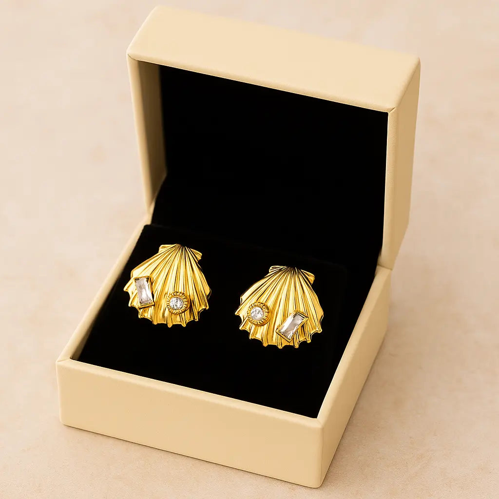 Gold shell-shaped earrings with gemstones in a beige box on a beige background