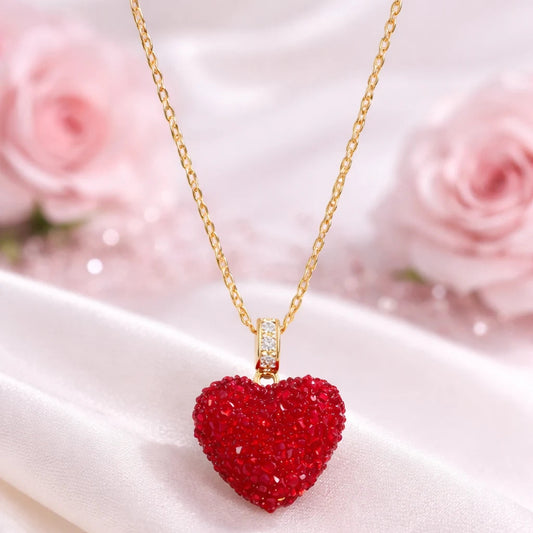 Red heart-shaped pendant necklace on a gold chain with pink roses in the background