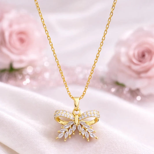 Gold butterfly necklace with diamonds on a white satin background with pink roses.