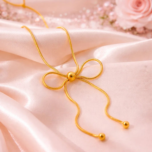 Gold necklace with a bow on a pink satin background