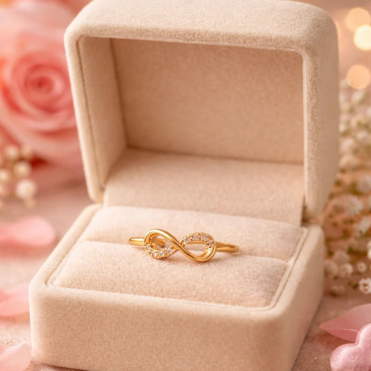 Gold ring with infinity symbol in a beige jewelry box on a soft pink background with flowers.