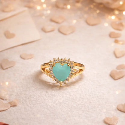 Gold ring with a turquoise heart-shaped gemstone on a soft background with lights and ribbons.