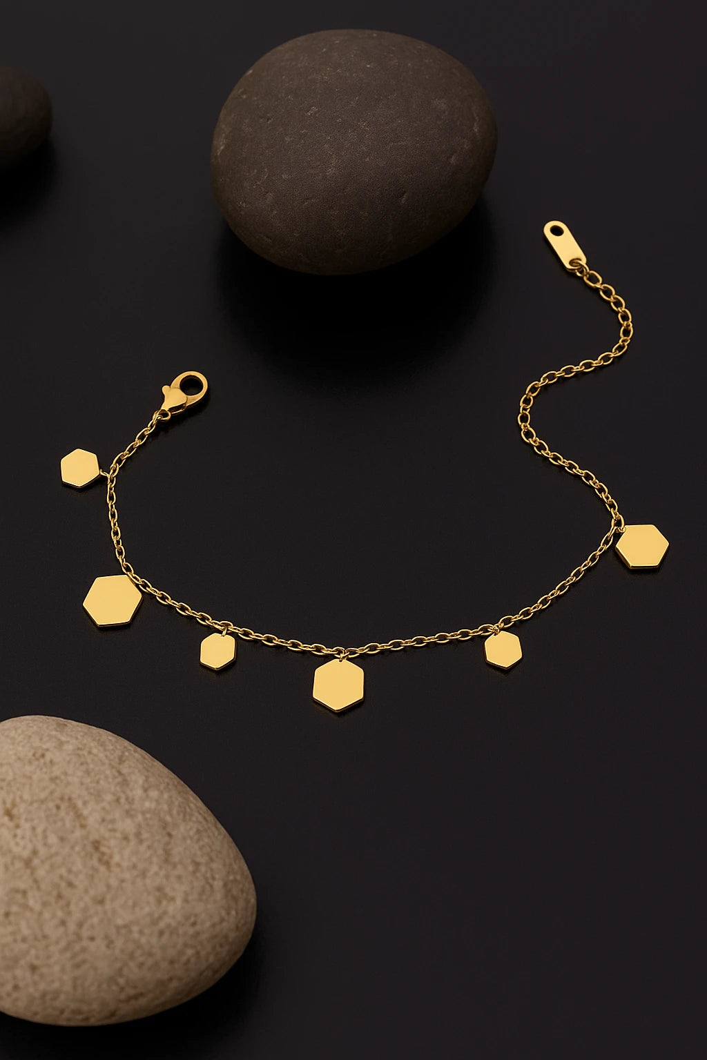 Gold bracelet with hexagonal charms on a dark surface with stones.