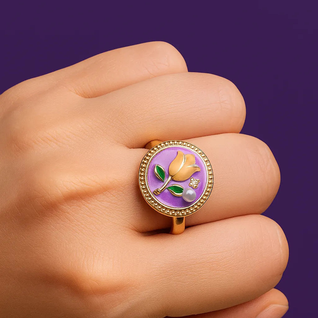 Gold ring with a purple gemstone and floral design on a hand against a purple background