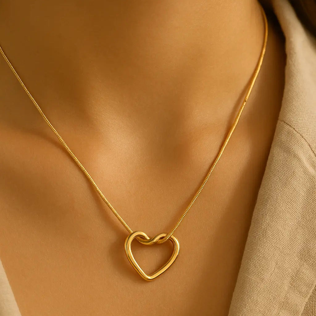 Gold heart-shaped necklace on a person wearing a beige top.