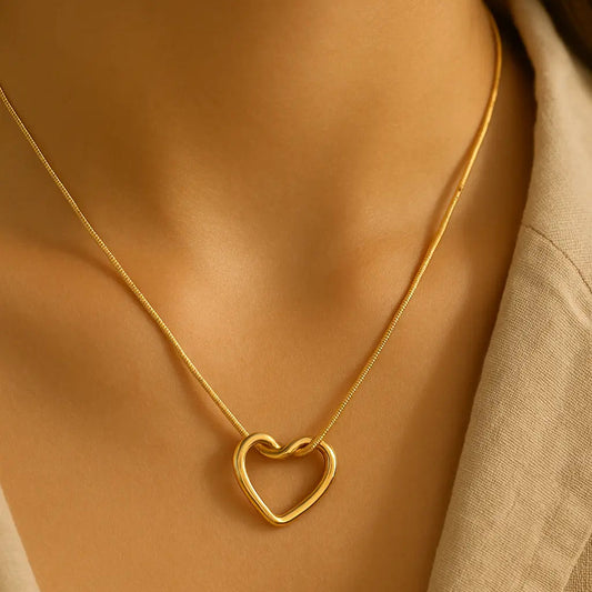 Gold heart-shaped necklace on a person wearing a beige top.