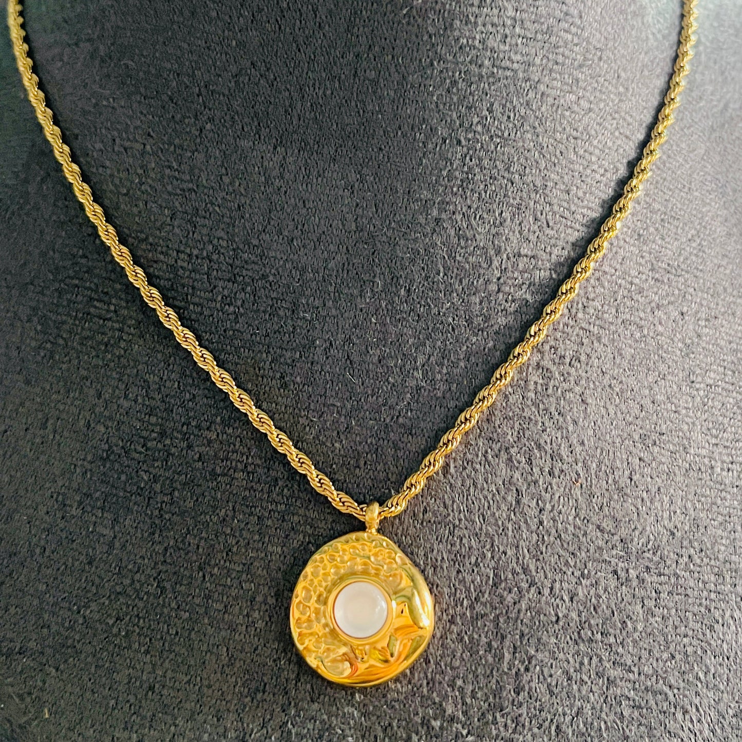 Gold necklace with a pendant on a mannequin bust.