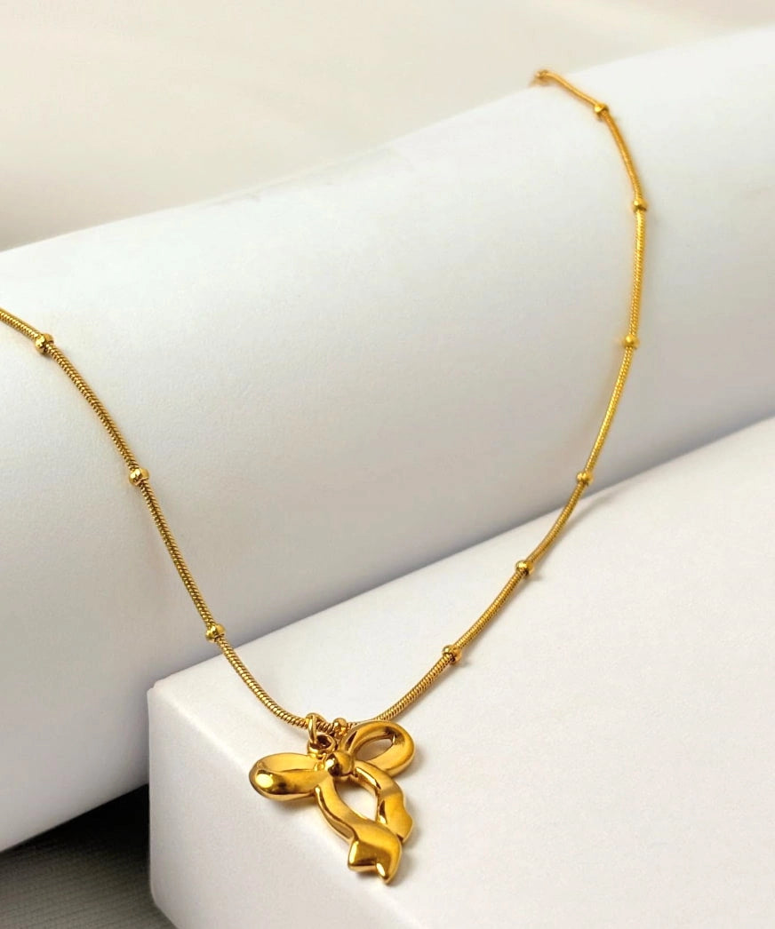 Gold necklace with a bow pendant on a white surface