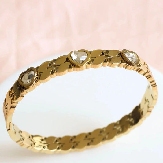 Gold bracelet with heart-shaped gemstones on a white surface