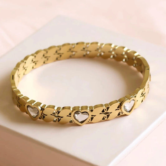 Gold bracelet with heart designs on a light pink surface