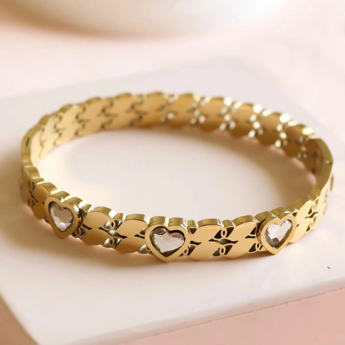 Gold bracelet with heart designs on a light pink background