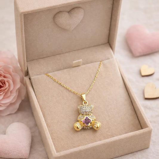 Gold teddy bear pendant necklace in a jewelry box with pink flowers and hearts on a soft background