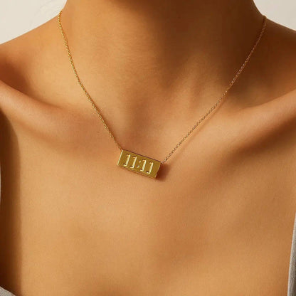 Gold necklace with a rectangular pendant on a person's neck against a neutral background