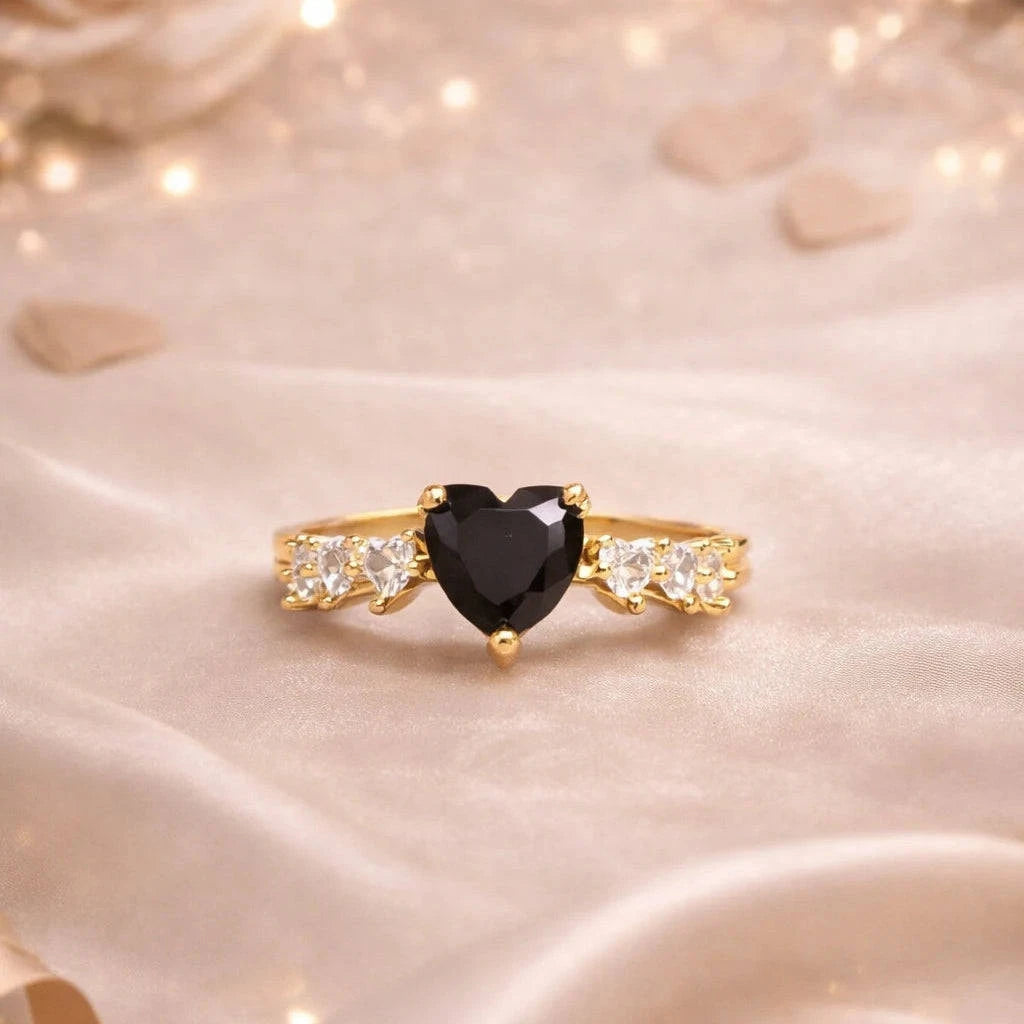 Gold ring with a black heart-shaped gemstone on a soft, light-colored fabric background.