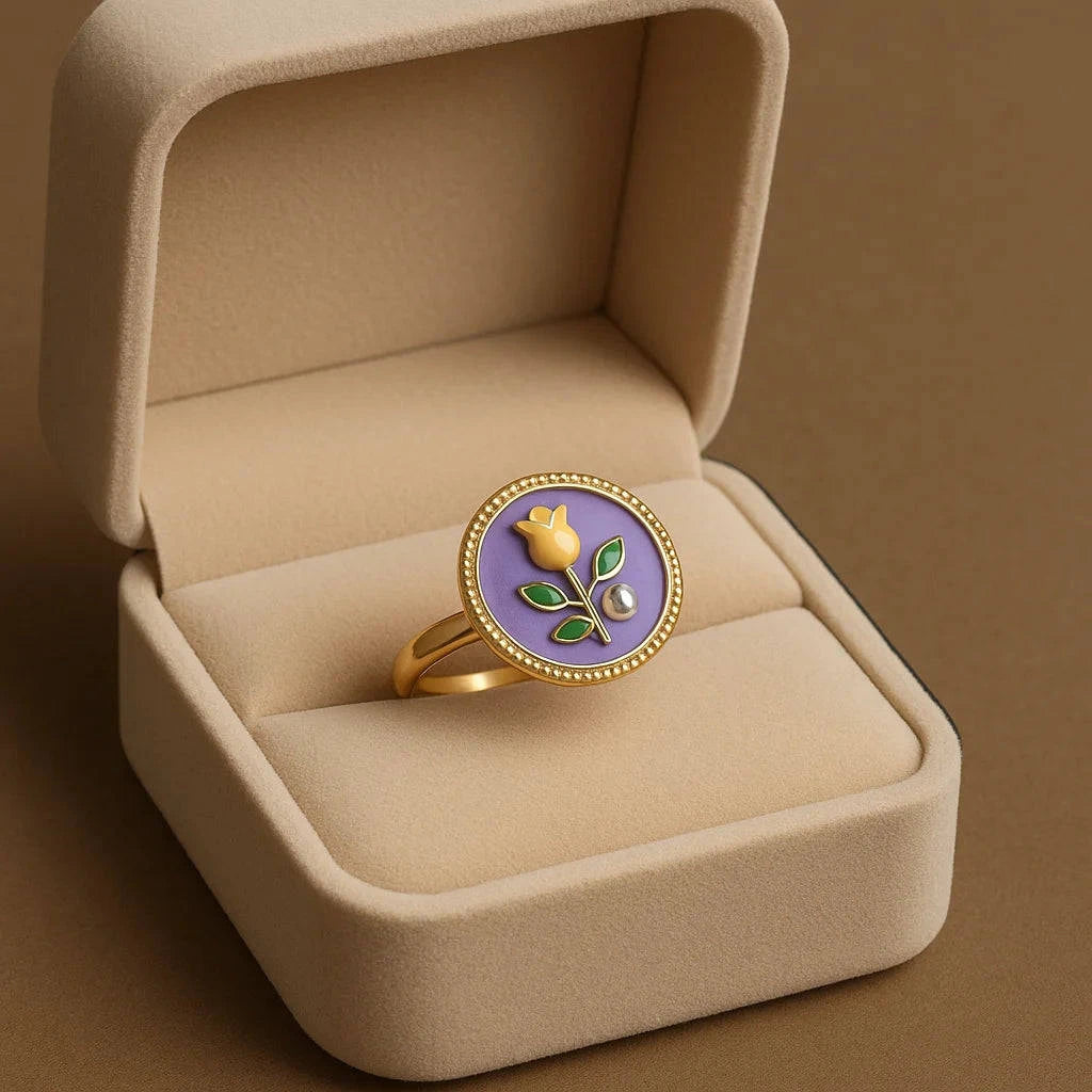 Gold ring with a purple stone and floral design in a beige jewelry box.